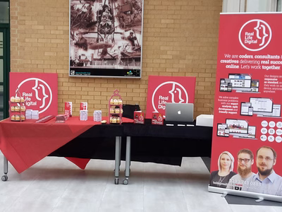 The Real Life Digital stand before the crowds arrived - a long table with giveaways and cupcakes on it. In the background are two large Real Life Digital logos printed on to canvas and to the right is a pop up banner featuring some of Real Life Digital's work.