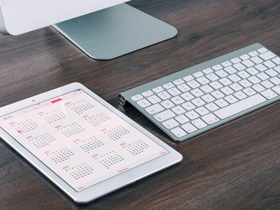A calendar app open on an ipad laying on a desk next to an imac, keyboard and mouse.