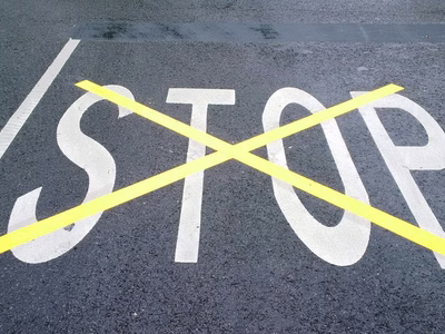 STOP painted on tarmac in white paint which has then been overpainted and crossed out with a large yellow 'X'.
