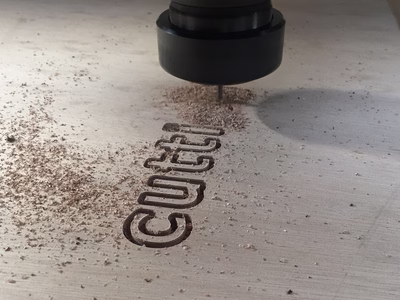 A CNC cutting machine is routing the word 'cutting' in to a sheet of wood.