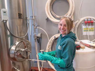 Smiling lady in factory stood next to a metallic vessel