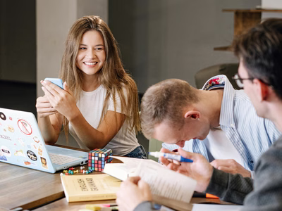 A woman smiles at her colleague as another man laughs as they collaborate on a project.