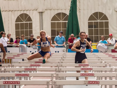 Four female hurdle sprinters are leaping over the hurdles along the race track.