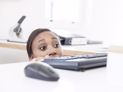 Businesswomen looking out for her boss peeking over desk with apprehesion.