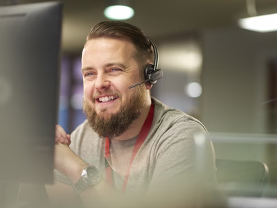 A smiling man speaking with a client via a headset.