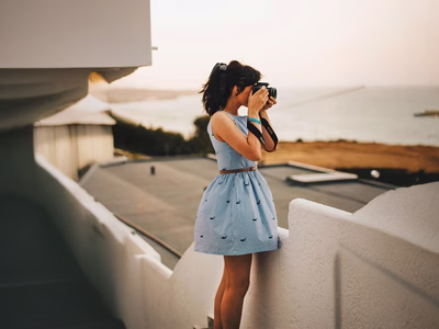A woman photographer wearing a blue sleeveless dress takes a photograph for a free stock photography website.