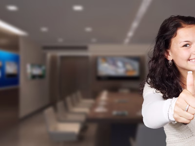 A lady with brown hair and a big smile is giving the thumbs-up to the camera.