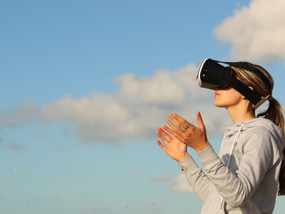 A woman wearing a virtual reality headset on a backdrop of a cloudy blue sky.