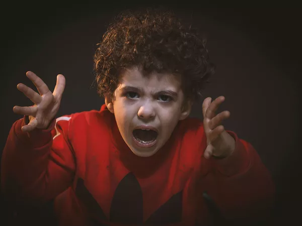 Boy expressing anger with a shouty face and outstretched hands.