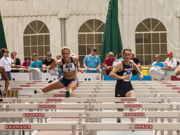 Four female hurdle sprinters are leaping over the hurdles along the race track.