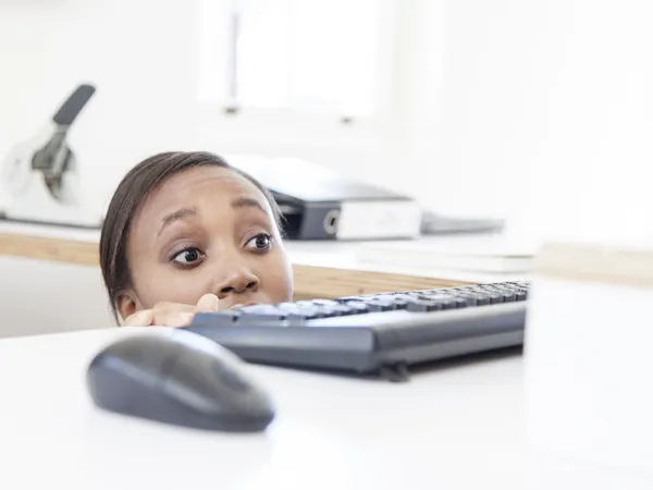Businesswomen looking out for her boss peeking over desk with apprehesion.