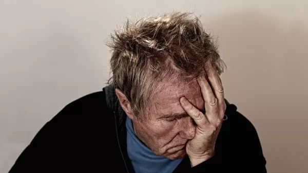 A middle aged man with blonde hair despairs with his hand over his face.