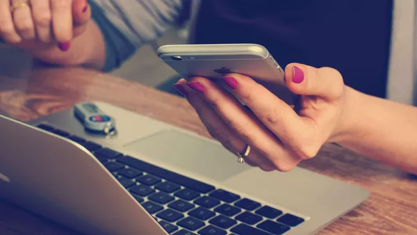 A lady looking on a phone and her MacBook.