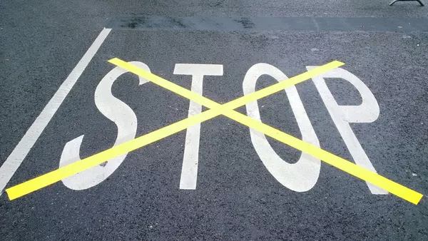 STOP painted on tarmac in white paint which has then been overpainted and crossed out with a large yellow 'X'.