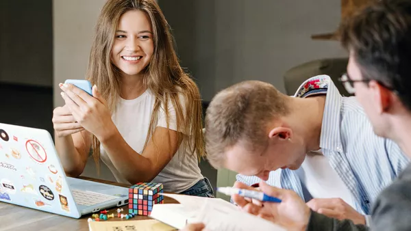 A woman smiles at her colleague as another man laughs as they collaborate on a project.