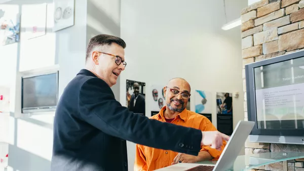 A business owner pointing at a laptop whilst talking with an employee.