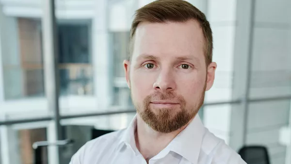 A man with neat hair and a beard looks intently at the camera.