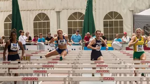 Four female hurdle sprinters are leaping over the hurdles along the race track.