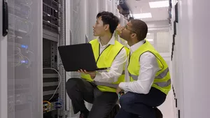 Two engineers knelt by a rack with a laptop performing maintenance.