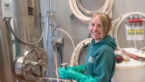 Smiling lady in factory stood next to a metallic vessel