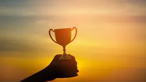 A trophy being held by a hand with a sunset background