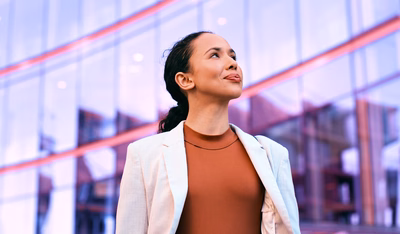 Confident businesswoman standing outdoors in front of a modern glass building, exuding professionalism and success.